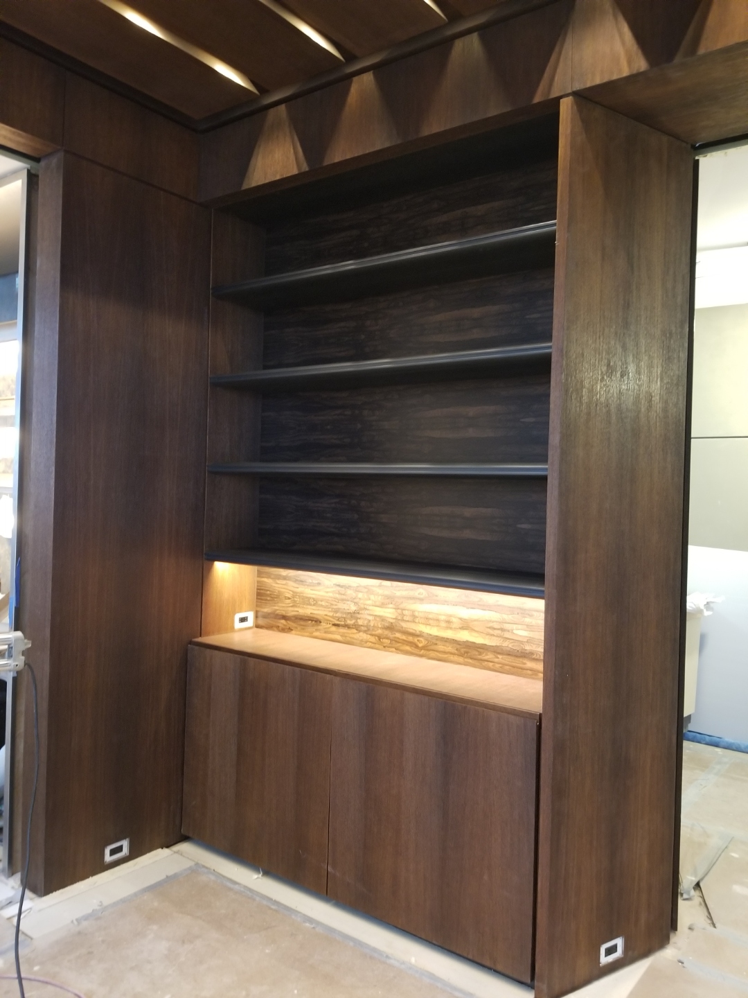 Bespoke media credenza and fluted walnut acoustic wall paneling with integrated fireplace surround in a Manhattan NYC apartment, blackened steel accents