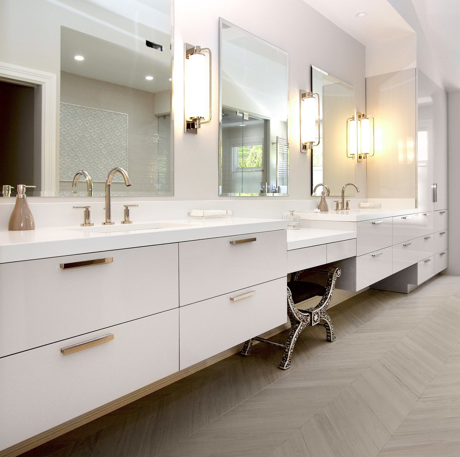 Real Modern Art Kitchen wall-suspended floating vanity with high-gloss white slab drawers, three-section his-and-hers layout with a lowered seated makeup station, undermount sinks, polished chrome bar pulls and wall-mount chrome faucets, over a herringbone tile floor